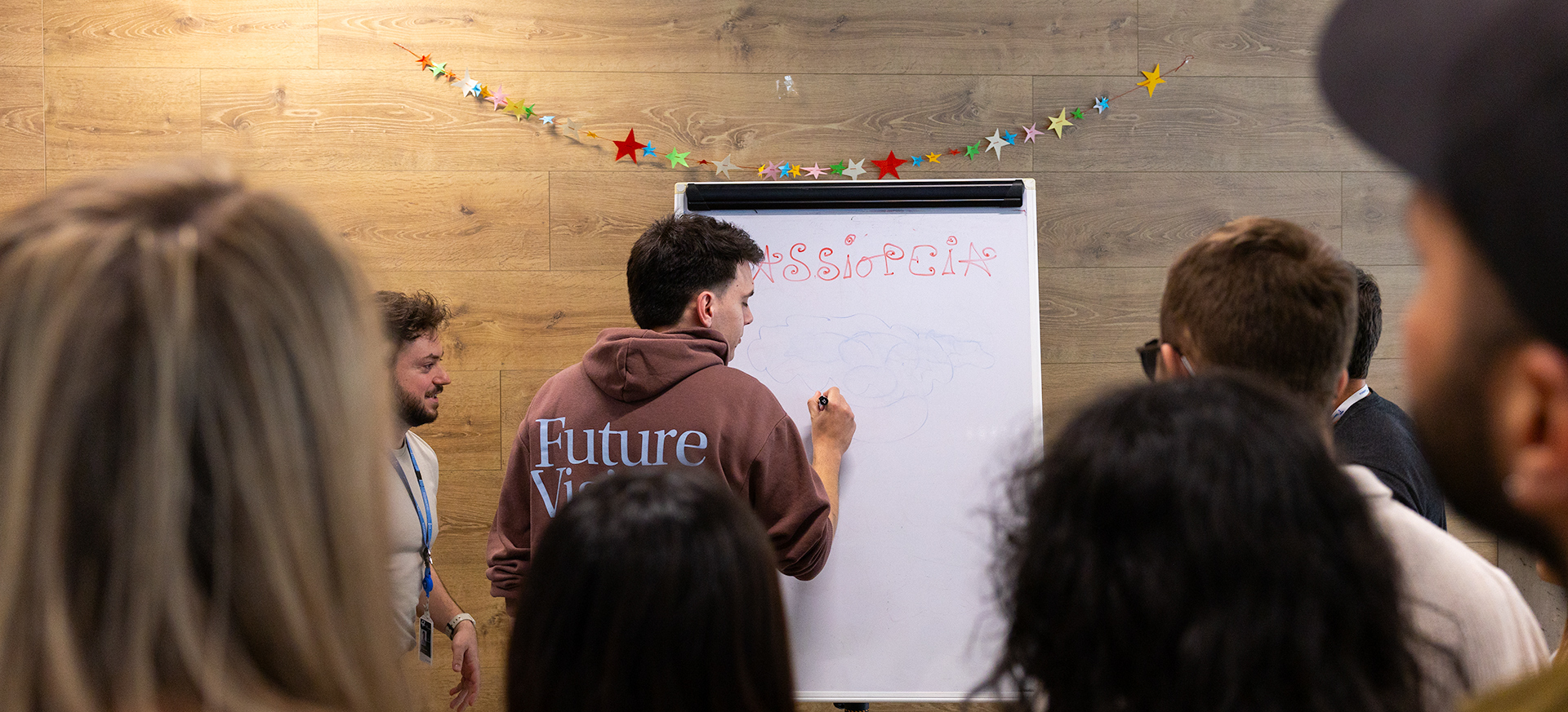 Estudiantes colaboran en grupo mientras uno de ellos escribe ideas en una pizarra durante una actividad en 42 Madrid Fundación Telefónica.