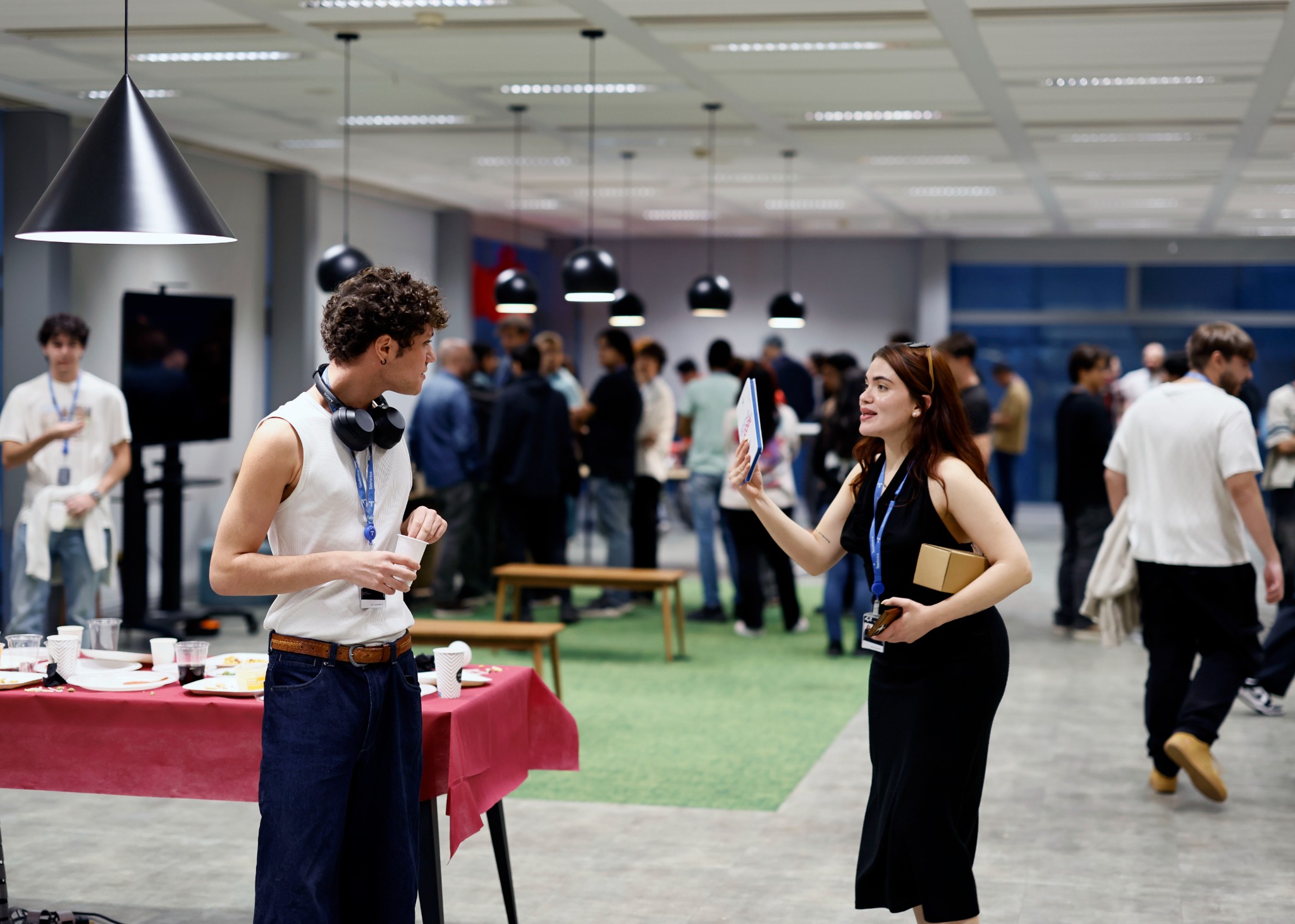Dos asistentes conversan durante la celebración del séptimo aniversario de 42 Madrid, con más participantes reunidos al fondo del campus.