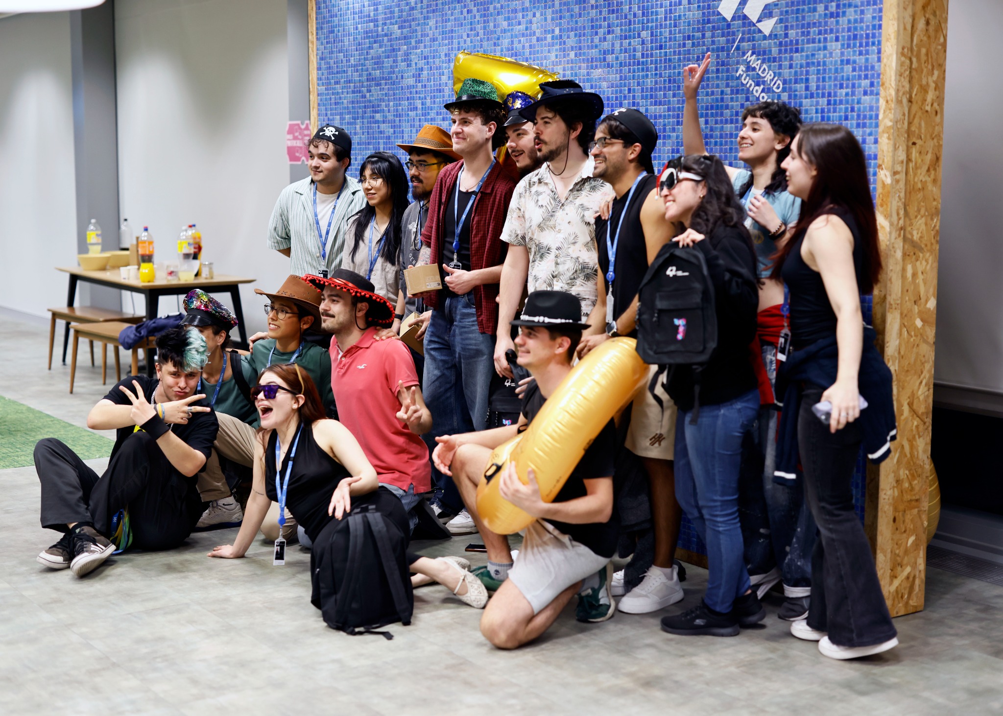 Group of friends posing for a photo at a party, wearing hats and lanyards indoors.